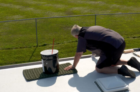 Person applying roof coating from a bucket on the roof with the help of RV Roof Magic Roof Coating.
