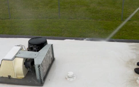 Person spraying a roof with cleaning solution near a vent and skylight.