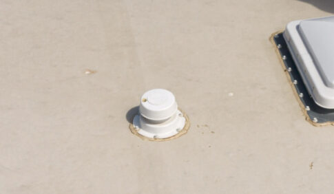 White vent pipe and skylight on a roof with a sealant ring.