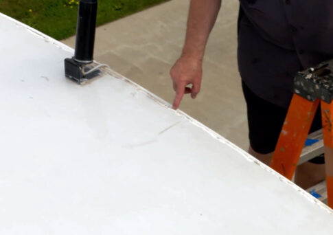 Close-up of a person pointing at a crack in a white roof coating.